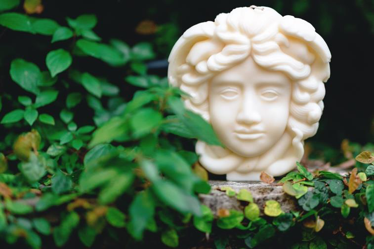 Candela scultorea YLOR a forma di busto classico, in cera d'oliva naturale, immersa nel verde